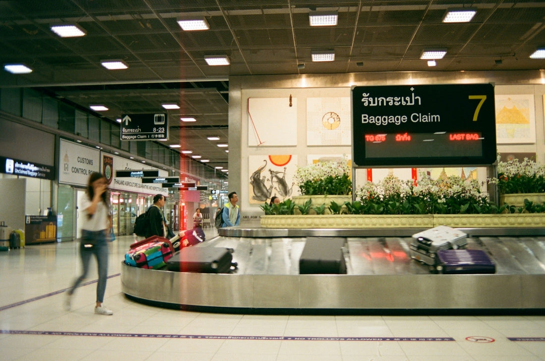 Travelers waiting beside an airport baggage claim carousel, where a luggage tracker for travel brings peace of mind
