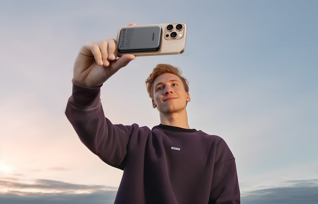 Man taking a selfie with a smartphone attached to a magnetic wireless power bank outdoors at sunset.