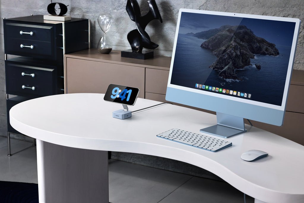 Smartphone charging on a compact charging dock beside an iMac on a modern office desk.